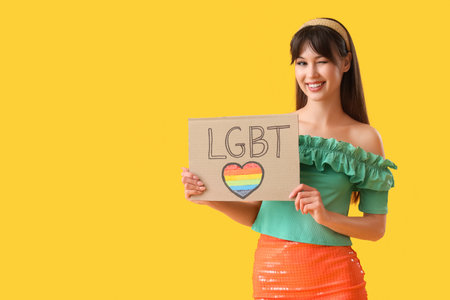 Beautiful young woman holding placard with word LGBT on yellow backgroundの写真素材