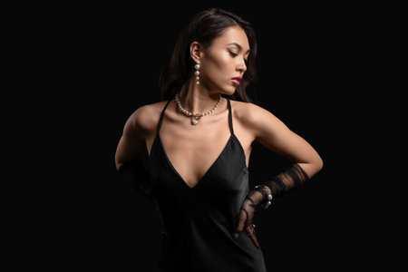 Beautiful young Asian woman with pearl jewelry on dark background