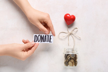 Jar with coins, red heart and hands with the word DONATE on light grunge background. Donation conceptの写真素材