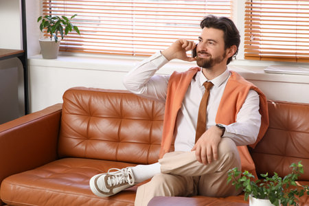 Handsome businessman working with mobile phone on couch in officeの写真素材