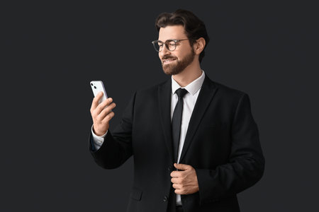 Handsome businessman in stylish suit with mobile phone on black backgroundの写真素材