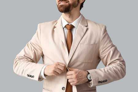 Handsome businessman buttoning beige jacket on light background, closeupの写真素材