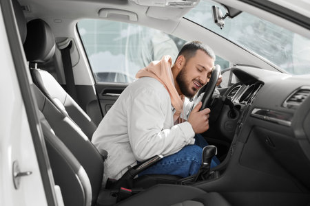 Handsome young man hugging steering wheel in car. I love my car concept