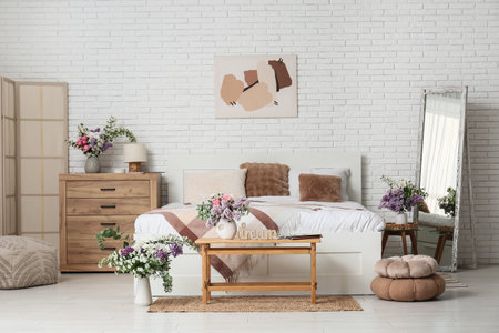 Vases with beautiful flowers in interior of light bedroomの写真素材