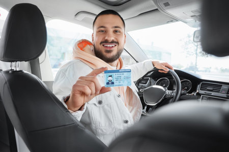 Handsome young male driver with driving license looking at passenger seat in car. I love my car...