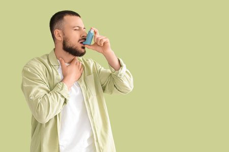 Young man with asthma attack using inhaler on green backgroundの写真素材