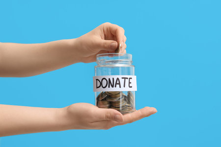 Hands holding jar with money on blue background. Donation concept