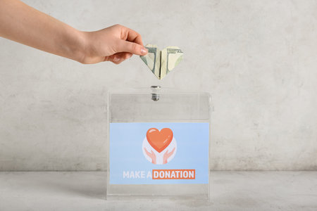 Hand putting money into box on light background. Donation concept