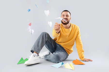 Young man with paper planes sitting on light background
