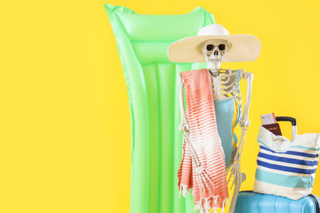 Human skeleton with beach accessories and suitcase on yellow backgroundの写真素材
