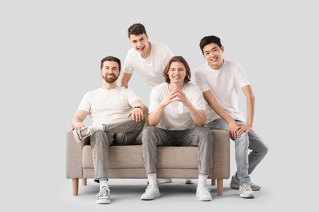 Group of young men in white t-shirts and with sofa on light backgroundの写真素材