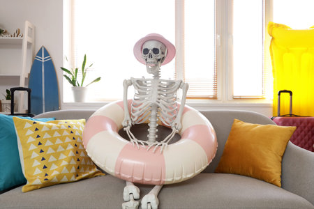 Human skeleton with summer hat and swim ring on sofa in living room