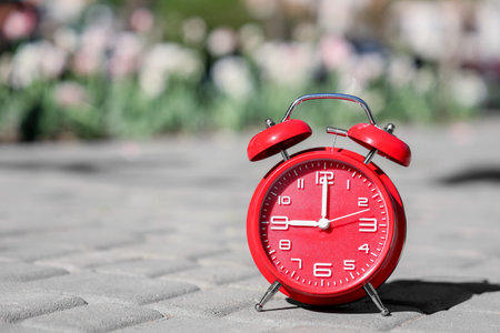 Red alarm clock on pavement outdoors, closeup
