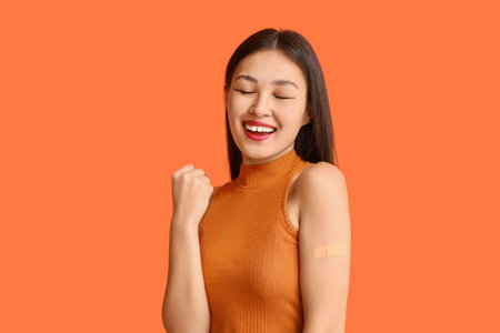 Happy Asian woman with applied medical patch on orange background. Immunization conceptの写真素材