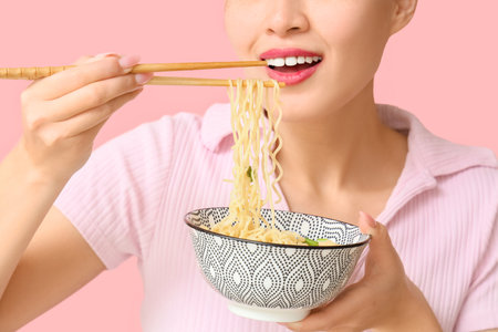 Young woman eating tasty ramen on pink background, closeupの写真素材