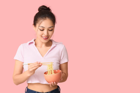Young Asian woman eating tasty ramen on pink backgroundの写真素材
