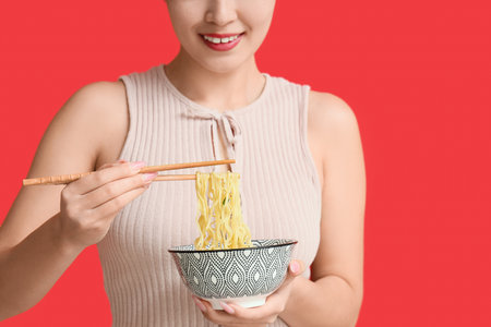 Young woman eating tasty ramen on red background, closeupの写真素材