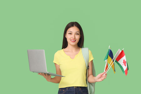 Young Asian woman with flags of different countries, backpack and laptop on green backgroundの写真素材