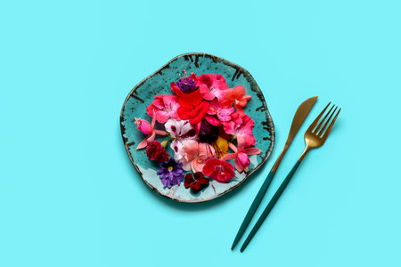 Plate with different beautiful edible flowers and cutlery on blue backgroundの写真素材