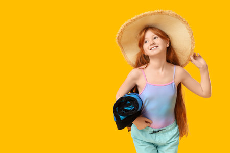 Little redhead girl with beach towel on yellow backgroundの写真素材