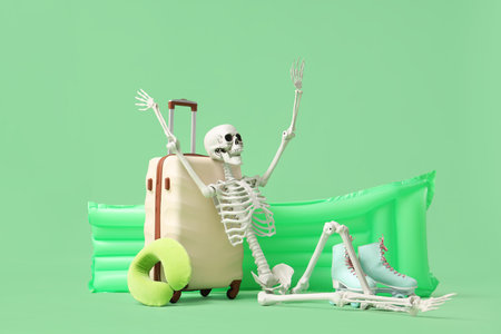 Human skeleton with suitcase, roller skates and swim mattress on green background. Travel conceptの写真素材