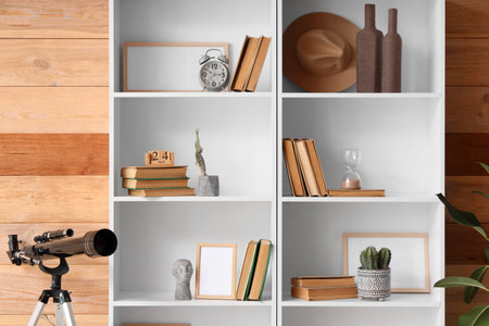 Bookshelf with decor, telescope and cacti near wooden wall in roomの写真素材