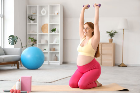 Sporty pregnant woman training with dumbbells at homeの写真素材