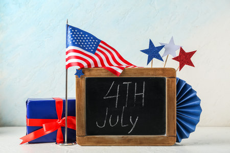 Chalkboard with text 4TH JULY, USA flag and gift box on table against white grunge background. Independence Day celebrationの写真素材