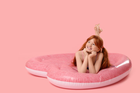 Little redhead girl lying on inflatable mattress against pink backgroundの写真素材
