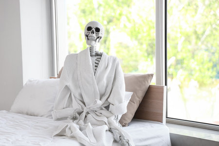 Human skeleton with bathrobe sitting in bedroomの写真素材