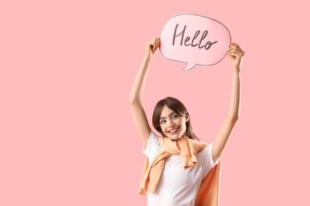 Young woman holding speech bubble with word HELLO on pink background