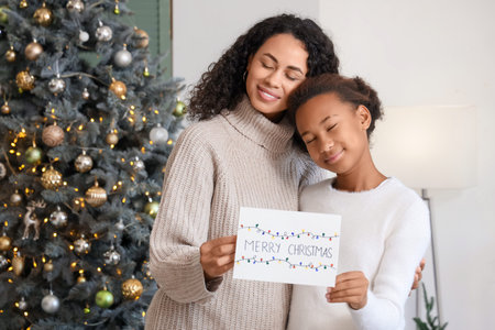 African-American mother and her daughter with greeting card hugging at home on Christmas Eve