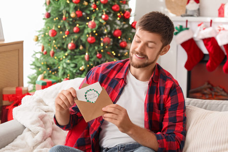 Young man with Christmas greeting card on sofa at homeの写真素材