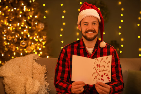 Young man in Santa hat reading Christmas greeting card on sofa at nightの写真素材