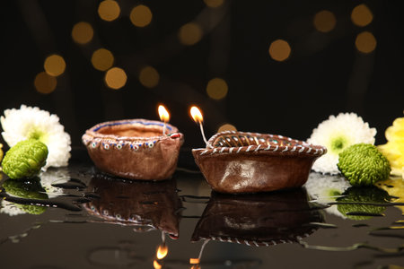 Diya lamps with chrysanthemum flowers in water on black background against blurred lights. Divaly...