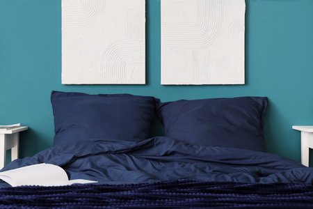 Bed with stylish blue bedding, pillows and hanging paintings on wall in bedroomの写真素材