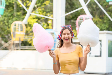 Beautiful young happy woman with different cotton candy near Ferris wheel in amusement park,...