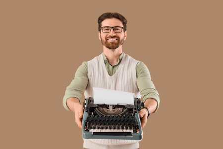 Young happy male writer with vintage typewriter on beige background