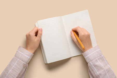 Female hands writing in notebook on beige background