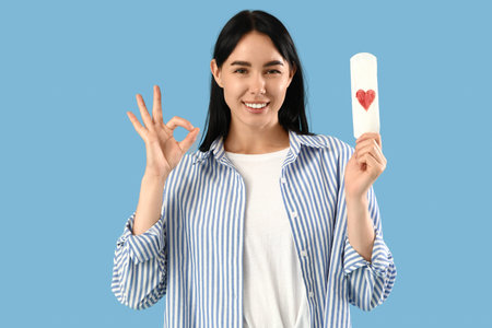 Young woman with menstrual pad showing OK on blue background