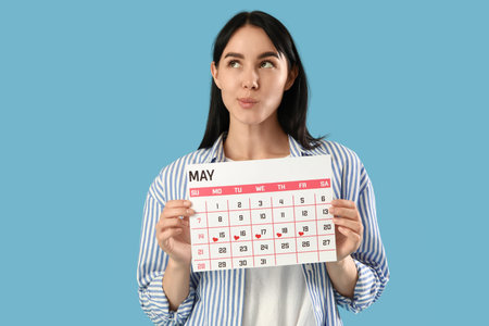 Thoughtful young woman with menstrual calendar on blue backgroundの写真素材