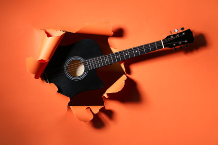 Black guitar visible through hole in orange paperの写真素材