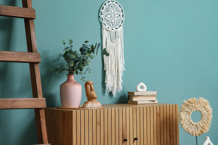 Vase with eucalyptus branches, statuette and books on commode in room
