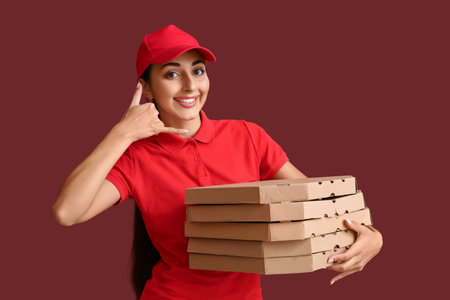 Female courier with pizza boxes showing "call me" gesture on burgundy backgroundの写真素材