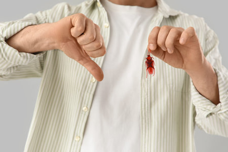 Young man with cockroach showing thumb-down on light background, closeup