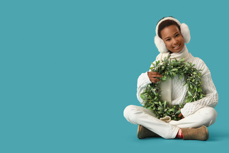 Teenage African-American girl with Christmas wreath sitting on blue backgroundの写真素材