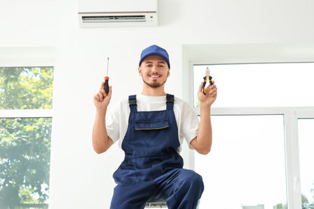 Male technician with repair tools near air conditioner in room