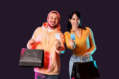 Young couple with shopping bags and credit cards on dark background.