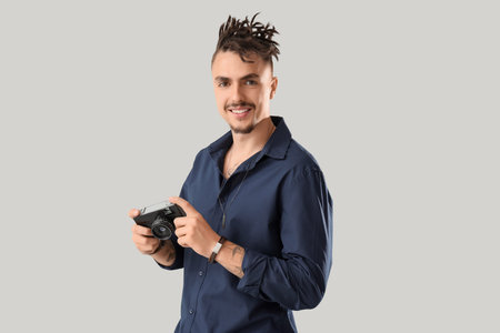 Young man with dreadlocks and photo camera on light background
