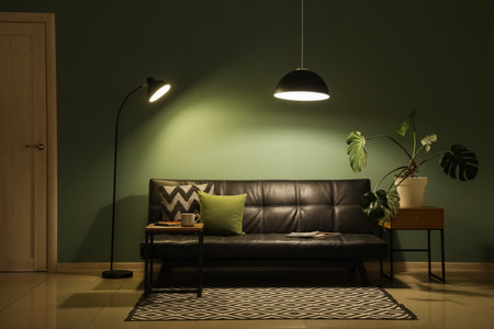 Interior of dark living room with black sofa, table and glowing lamps at night